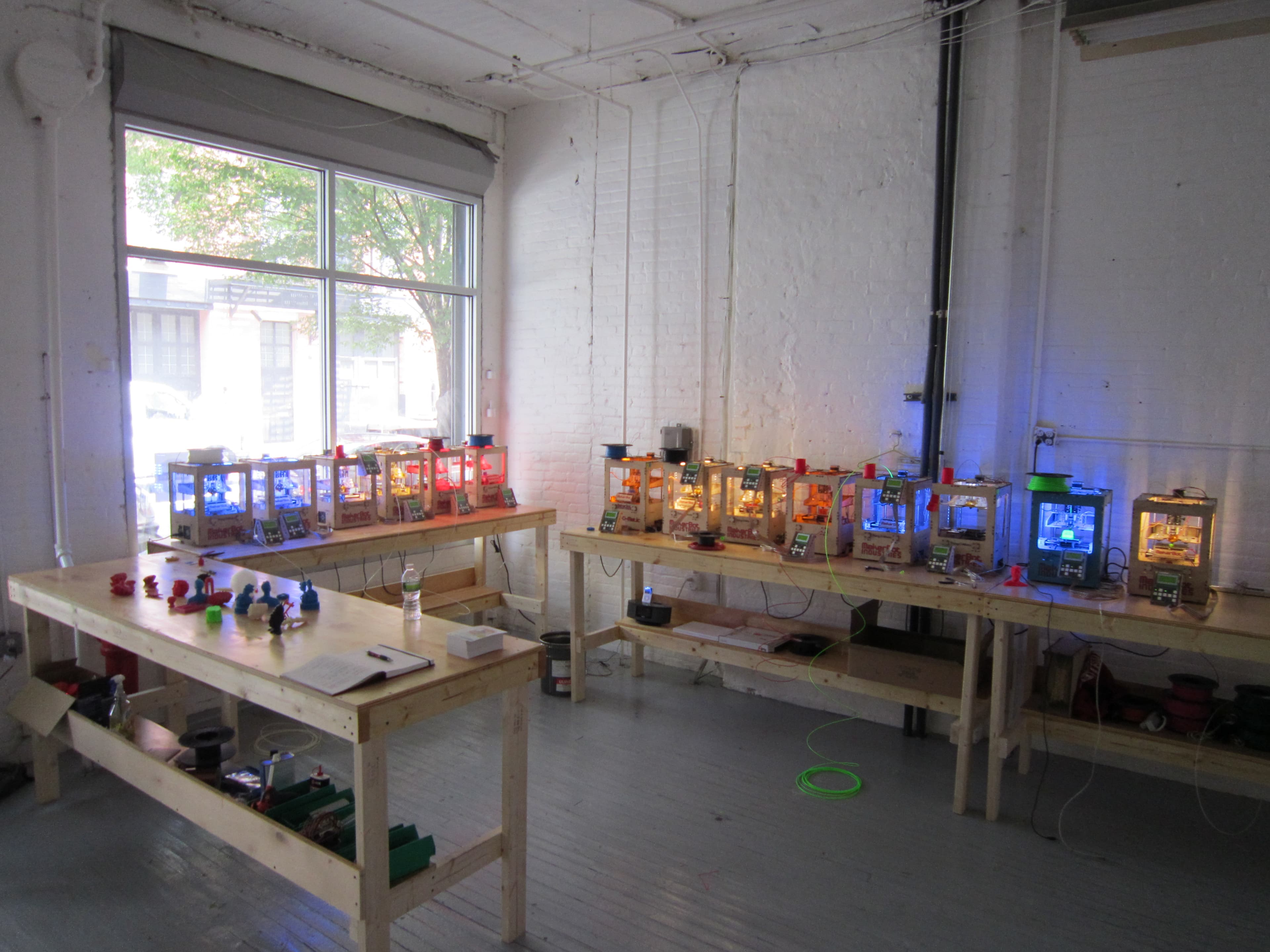 A small 3D printer farm with multiple printers running on workbenches.