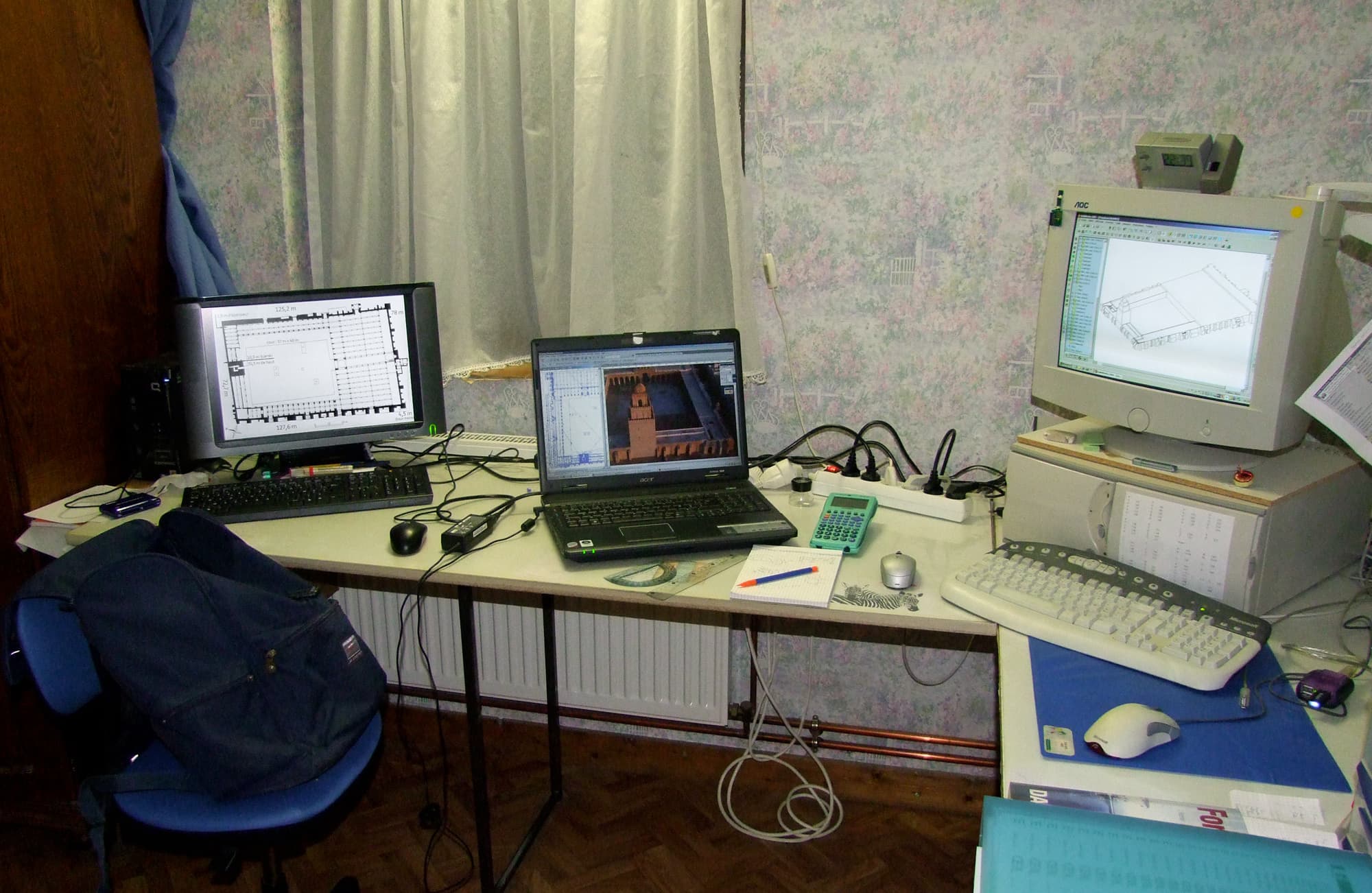 A CAD workstation with multiple screens showing technical drawings and models.