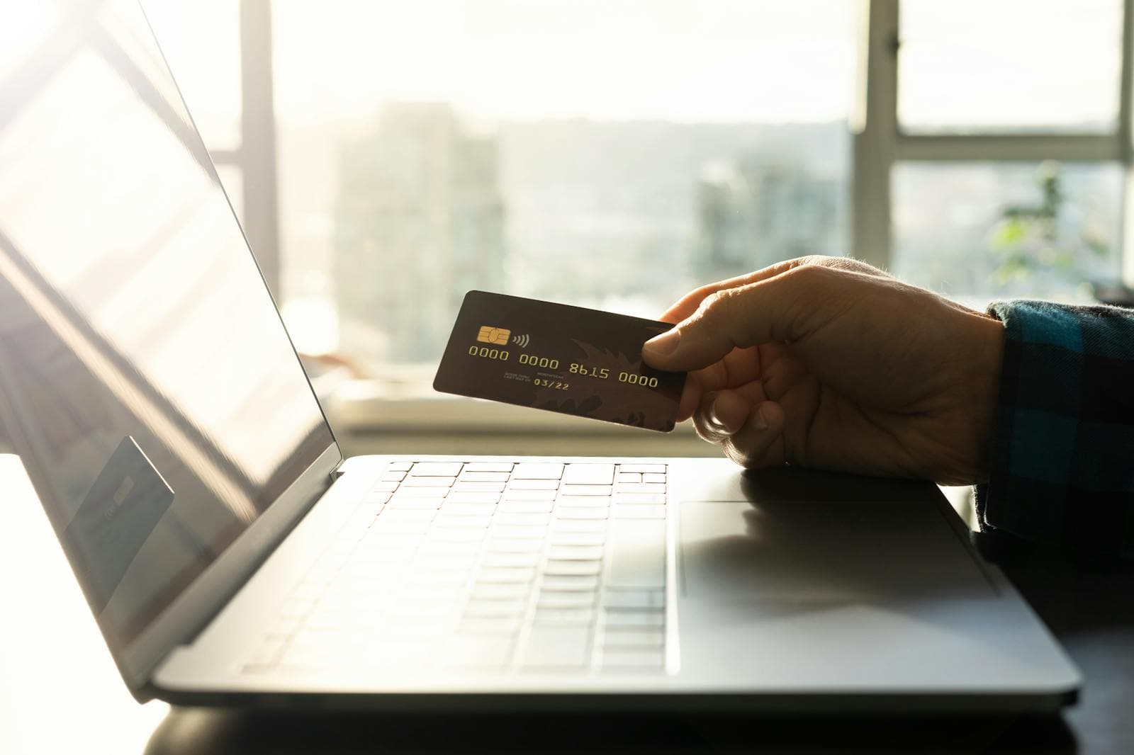 A credit card held near a laptop representing subscription payments and recurring SaaS costs.